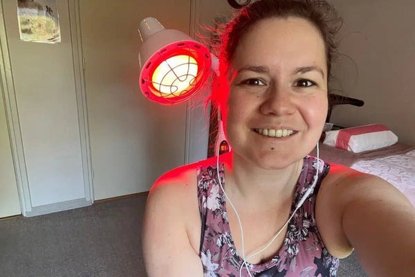 Vrouw glimlacht tijdens een infraroodlichttherapie sessie thuis met een rode infraroodlamp van Mvolo
