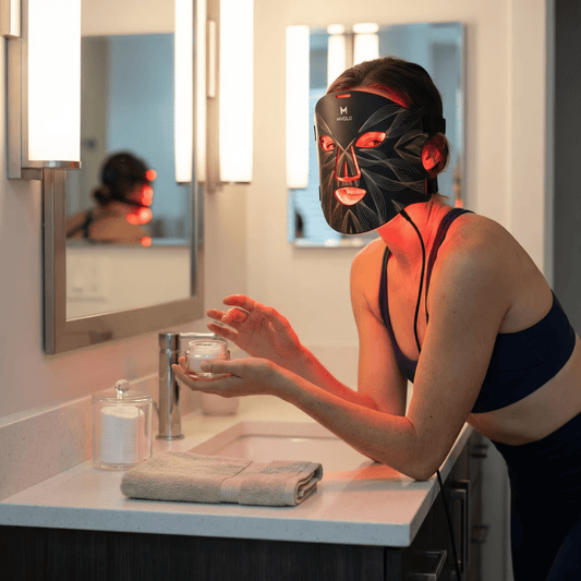 vrouw gebruikt een zwart Mvolo LED-gezichtsmasker in de badkamer als onderdeel van een anti-aging huidverzorgingsroutine thuis